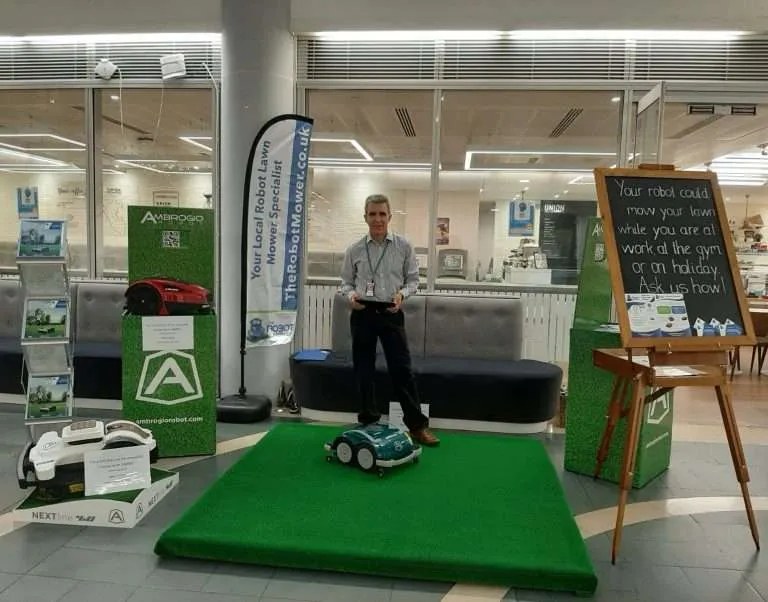 Indoor display showcasing robotic lawn mowers with a demo area and promotional signage.