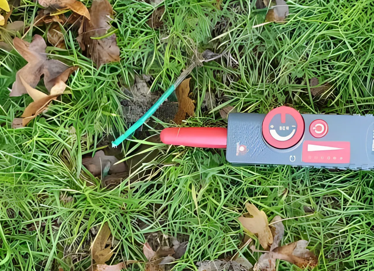 Close-up of a cable locator tool placed on grass, detecting a green buried wire.